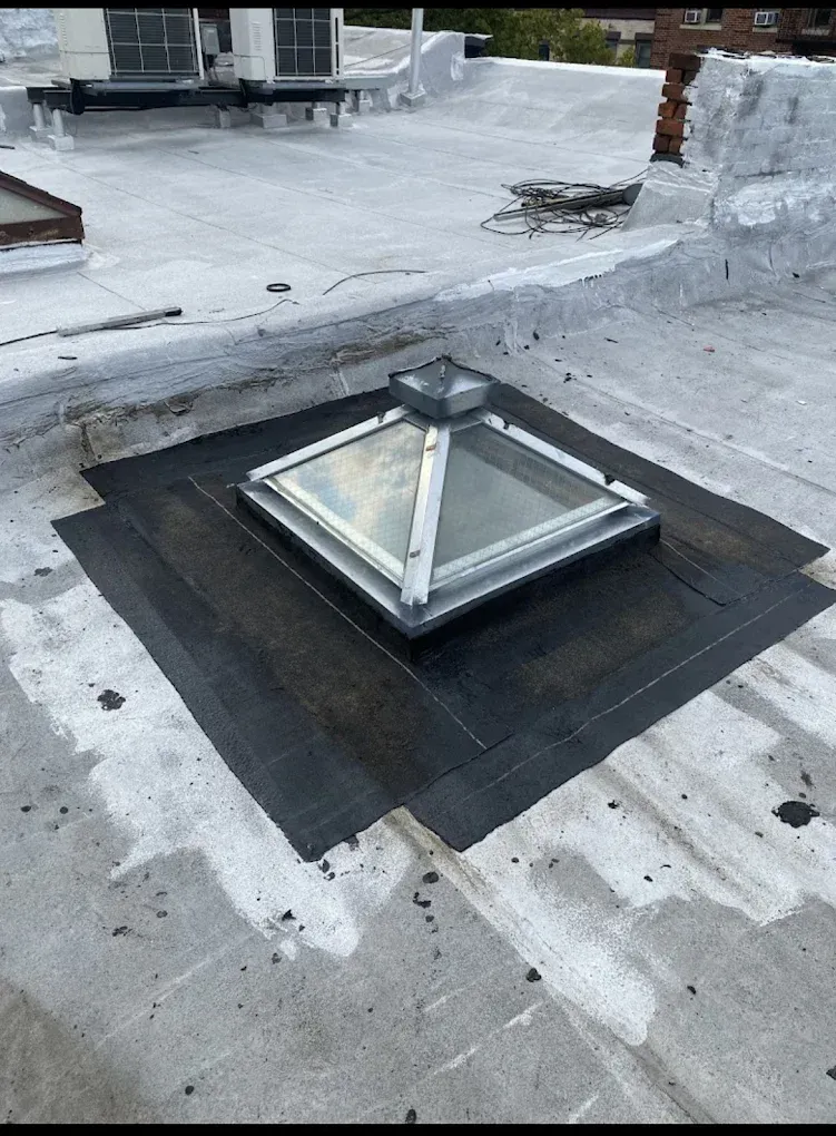 Rooftop skylight hatch on a flat roof, surrounded by black waterproofing membrane.