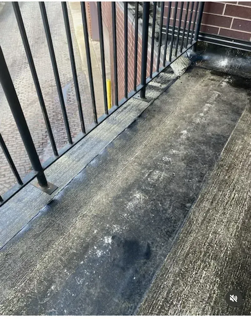 Wet concrete balcony with black metal railing and brick wall.