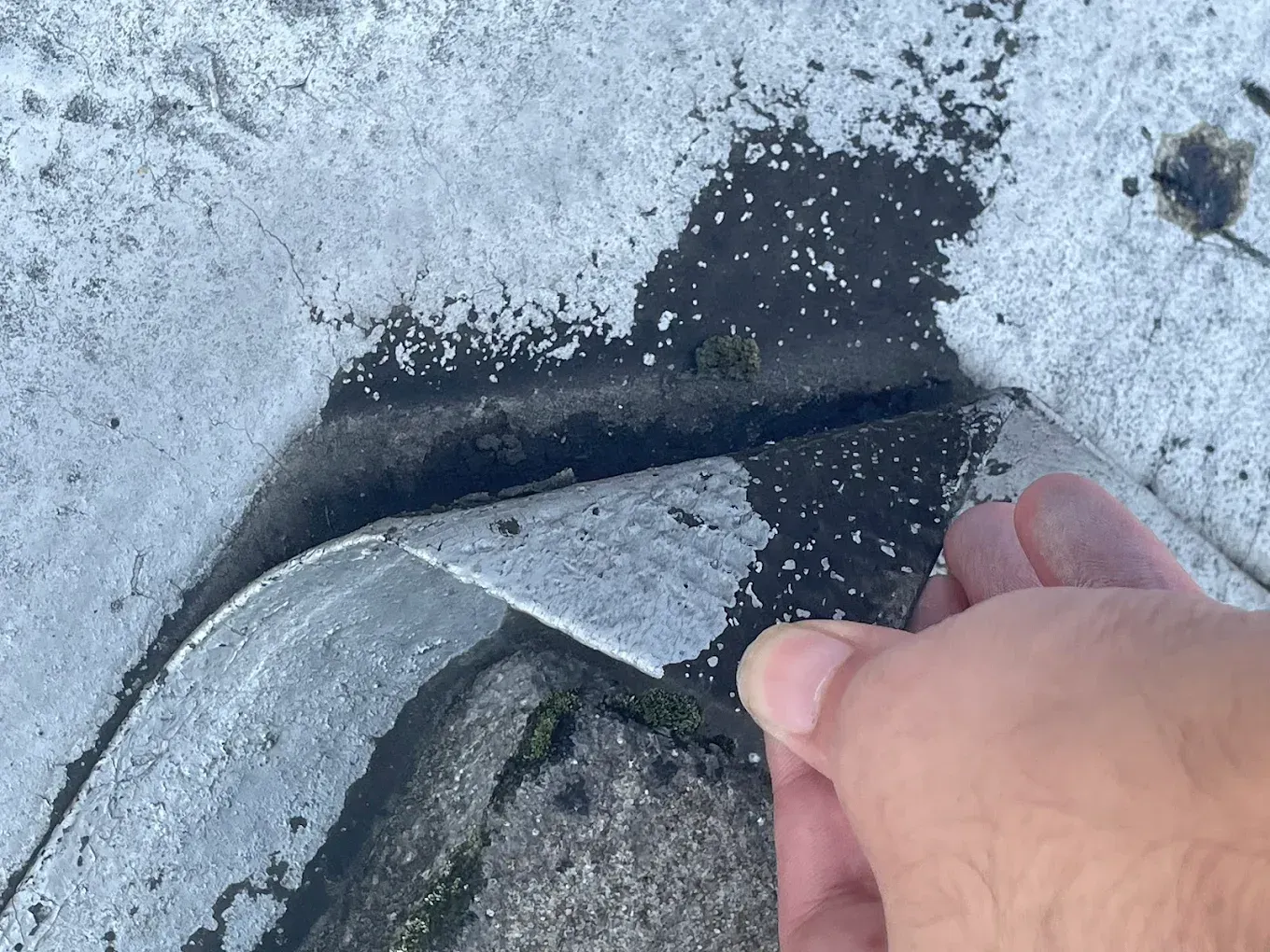 Hand peeling a black rubber strip from a cracked concrete surface