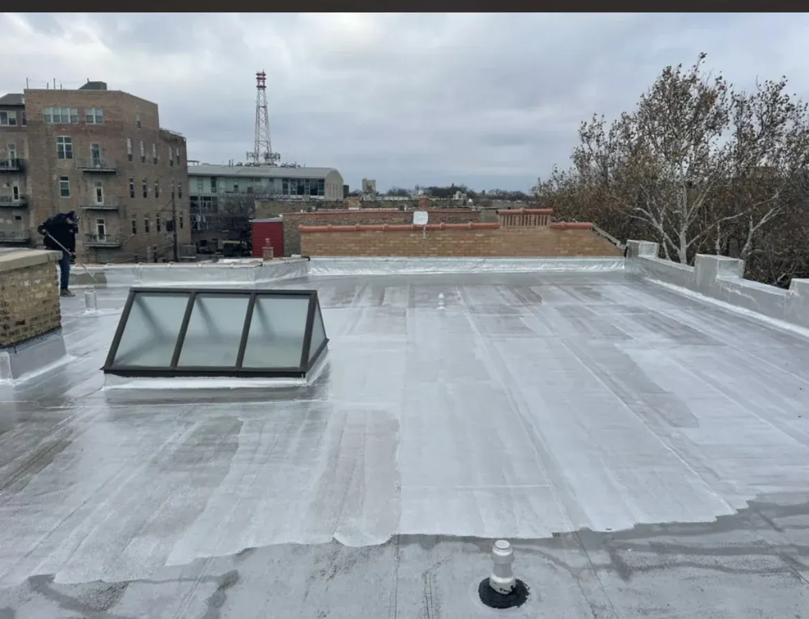 Rooftop with silver waterproof coating, skylight, and city buildings under a cloudy sky.