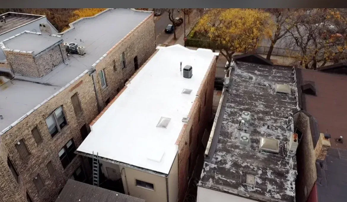 Aerial view of flat-roofed brick buildings with one bright white roof in an urban area.