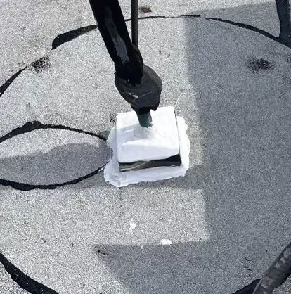 A person’s foot on a white rooftop vent, with dark gray cracked roofing around it.