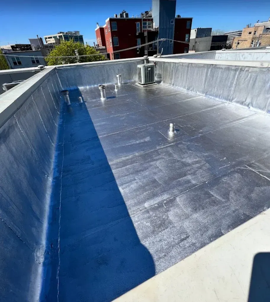 Sunny rooftop with silver waterproof membrane, blue parapet wall, and city buildings in the background