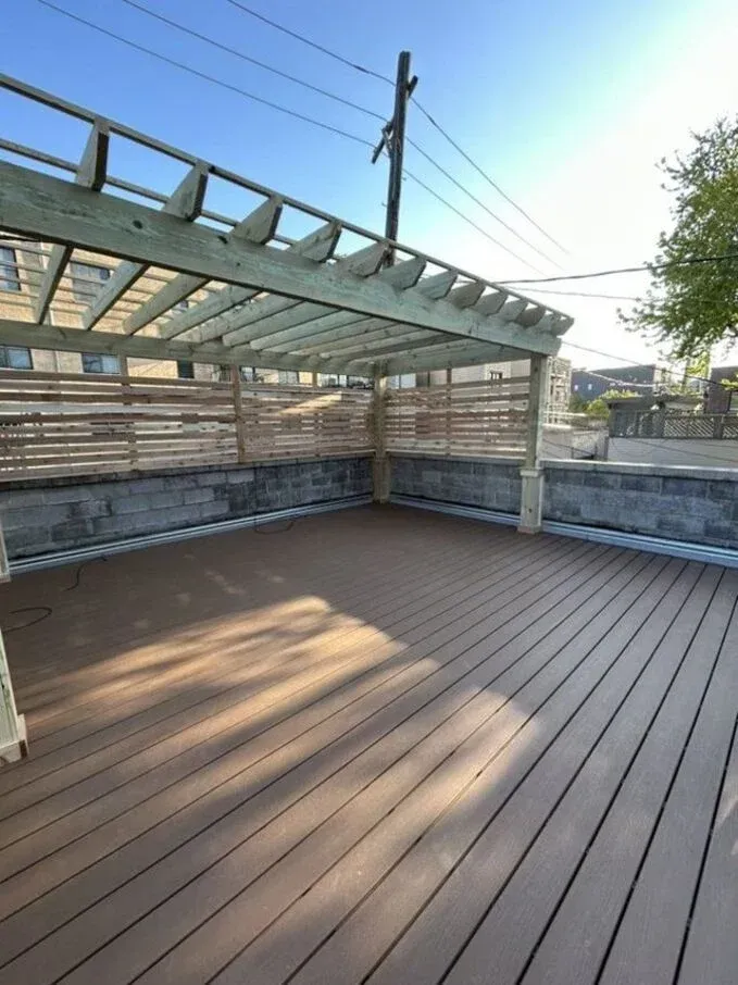 Empty wooden rooftop deck with slatted pergola and low stone walls in sunlight