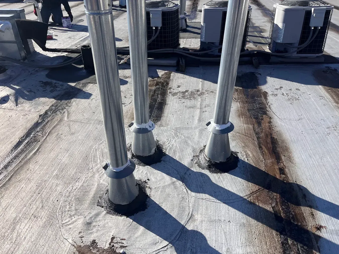 Metal pipes mounted on a rooftop with rust stains and angled shadows on the surface