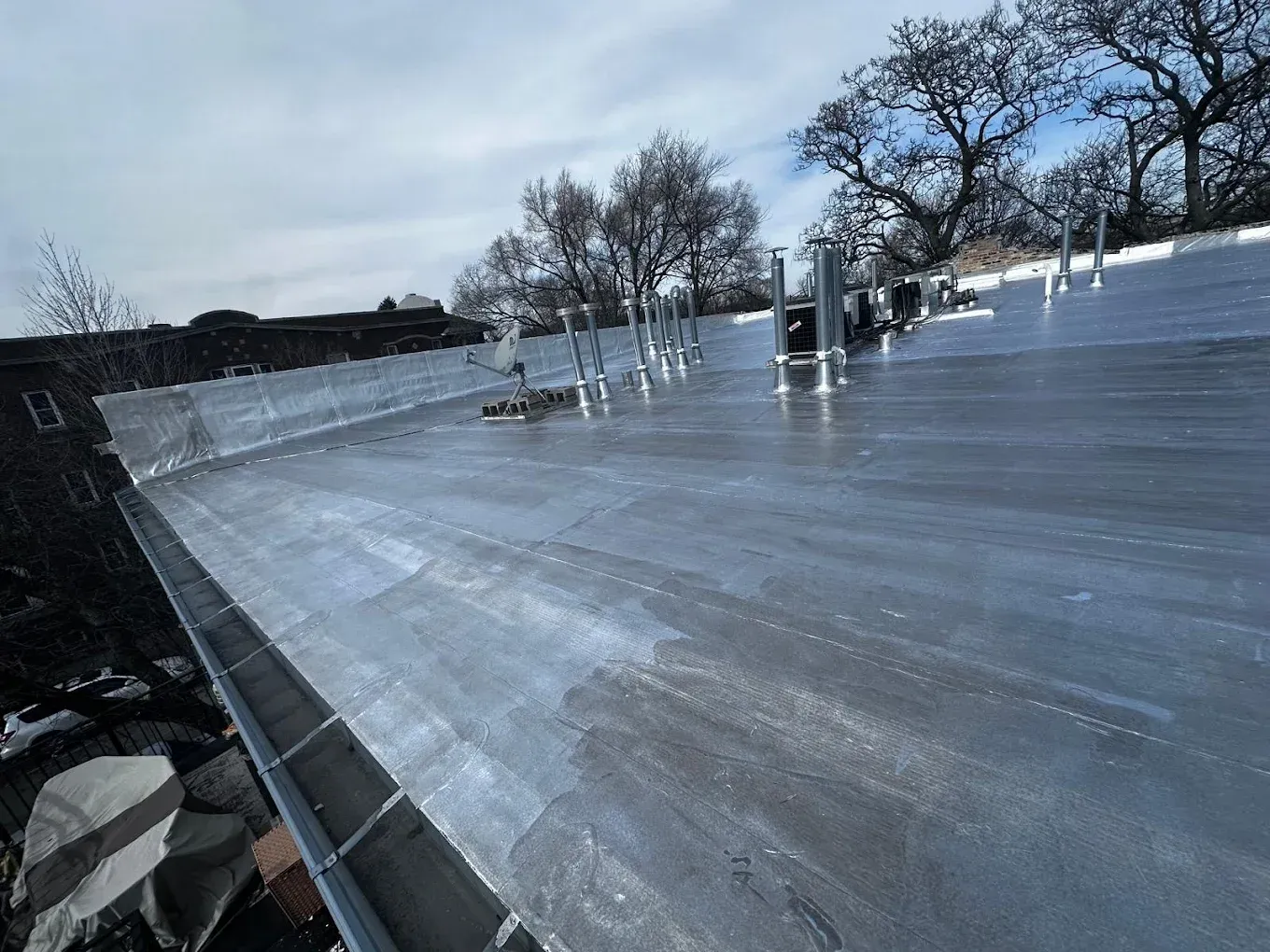 Flat rooftop with a thin layer of ice or snow under a cloudy sky, vents and trees in the distance