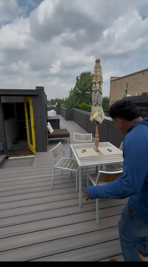 Person carrying a small table on a rooftop deck under cloudy skies.