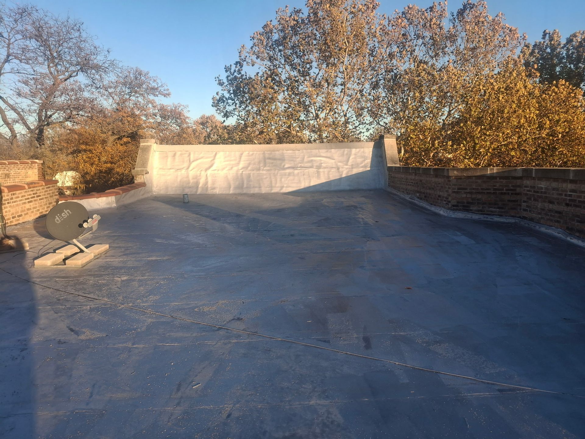 Empty rooftop at sunset with a low concrete wall and autumn trees in the background