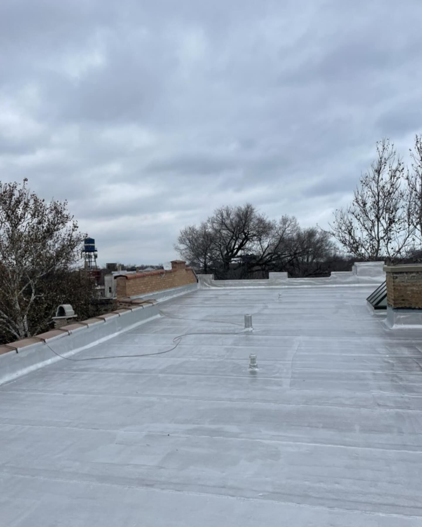 Flat silver rooftop under a cloudy sky, with trees and buildings in the background.