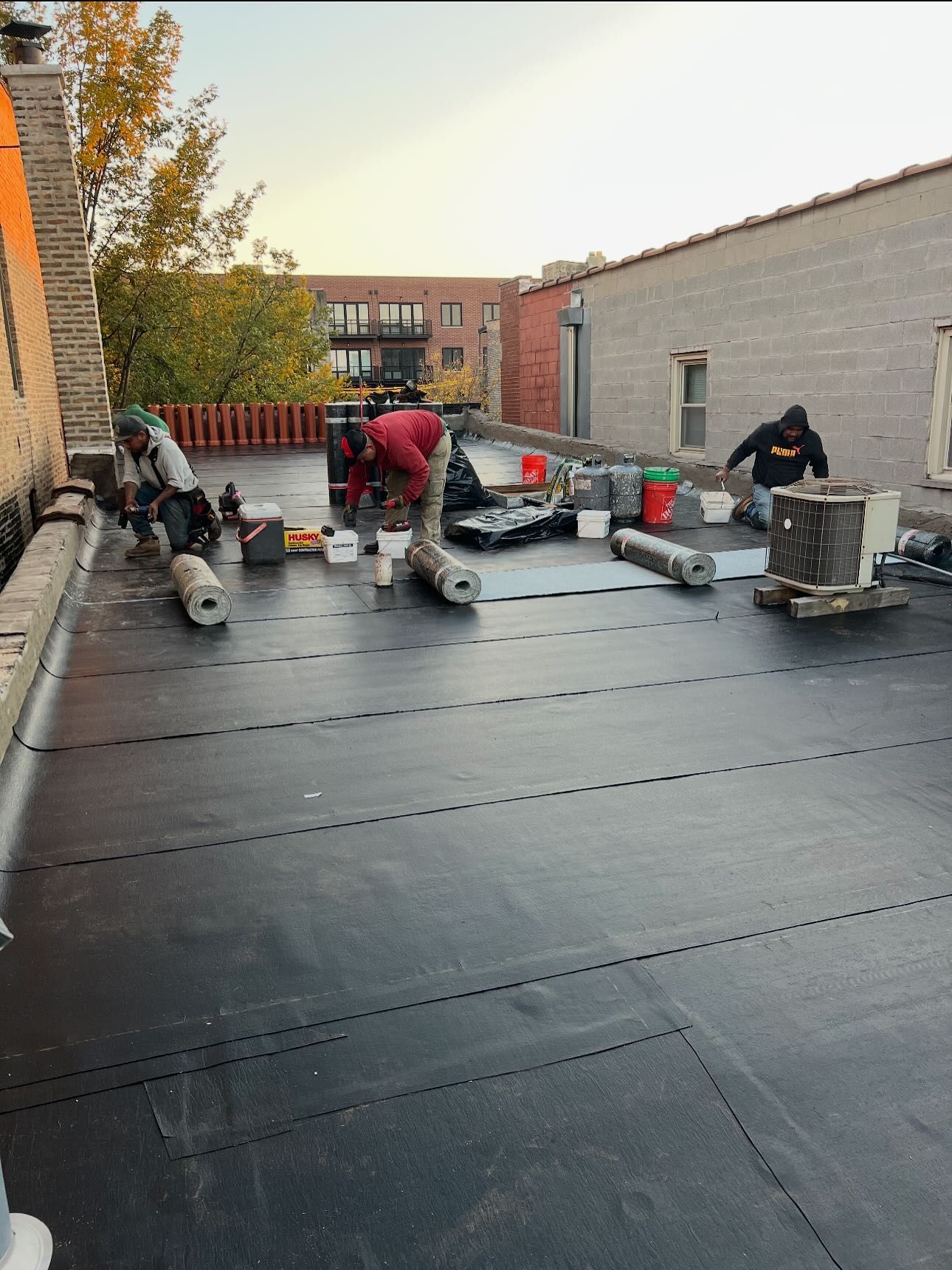 Workers installing black roofing membrane on a flat rooftop at a construction site