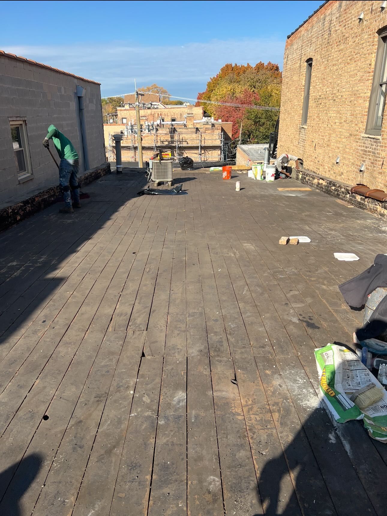 Rooftop with weathered decking, brick walls, and scattered construction materials under a blue sky