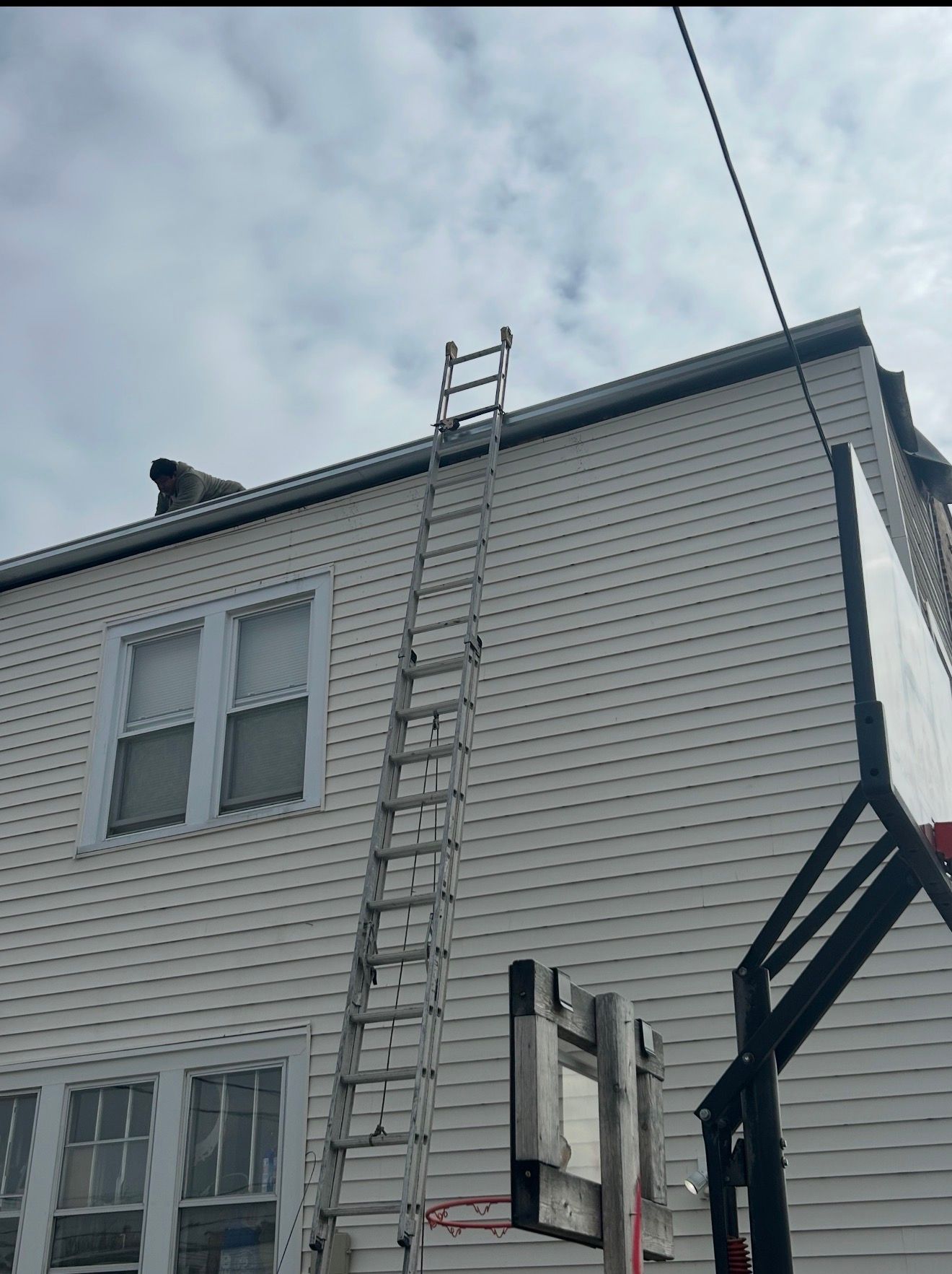 Ladder leaning against a white house exterior beneath cloudy sky, with an overhead utility wire nearby