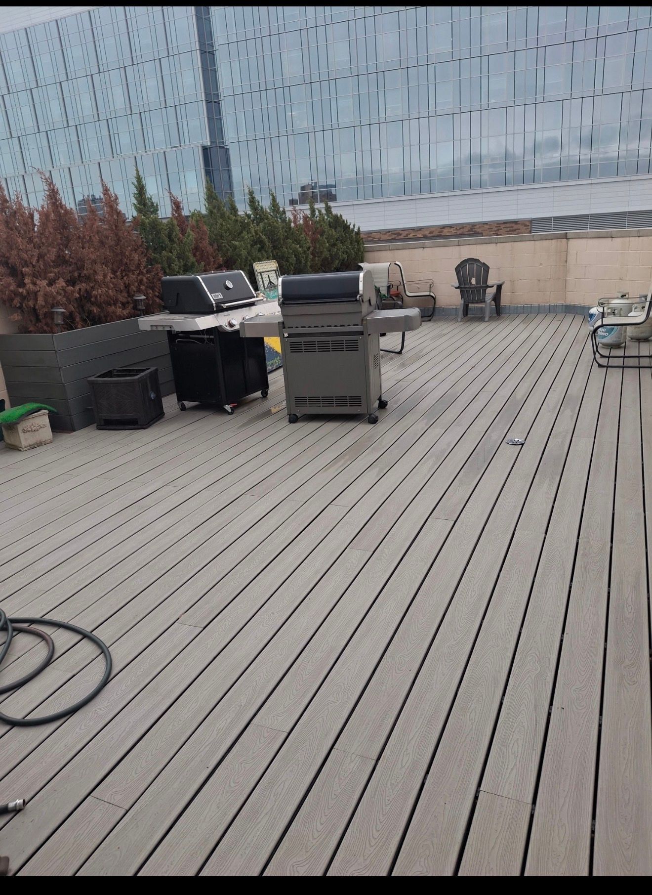 Outdoor deck with a grill, patio furniture, and a coiled hose beside a glass railing