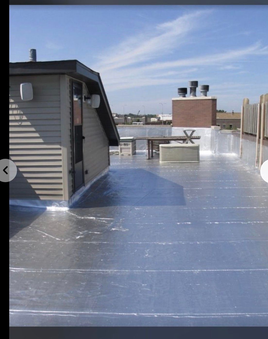 Rooftop deck with metallic floor, small shed, benches, and city skyline under a blue sky