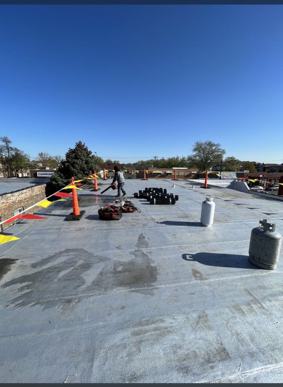 Flat rooftop with workers, HVAC units, tools, and safety cones under a clear blue sky