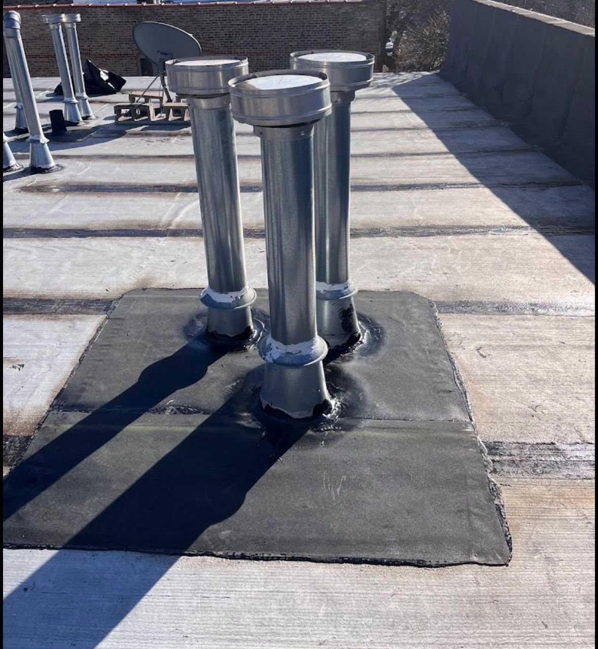 Three silver rooftop vents on a black sealed patch of flat roof in sunlight