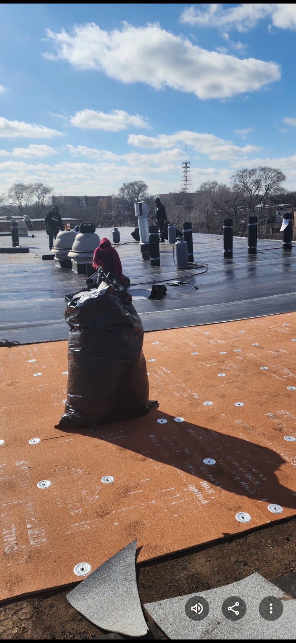 Snowy outdoor plaza with people near sculptures, wet orange pavement, and a cloudy blue sky