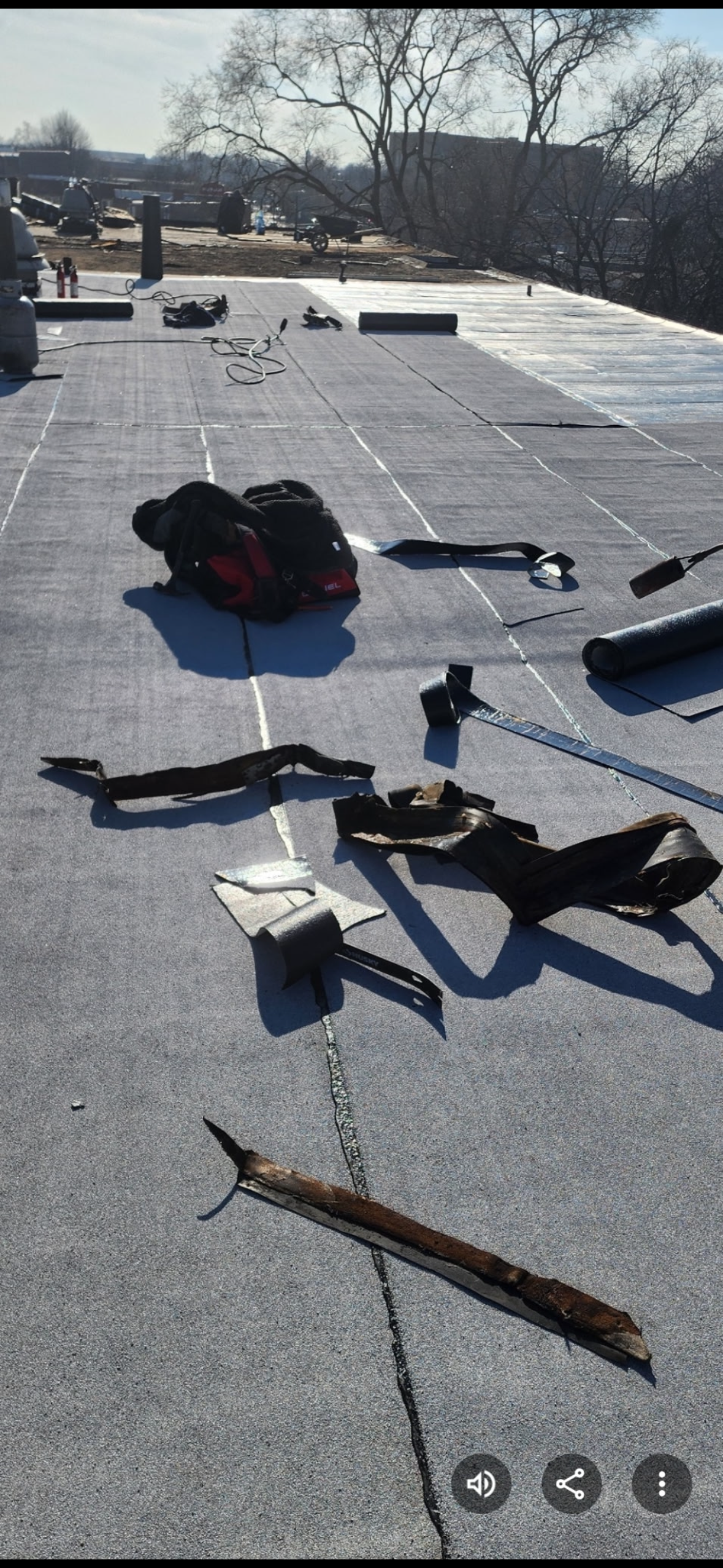 Scattered tools on a flat roof under bright sunlight, with trees and a distant hillside in the background