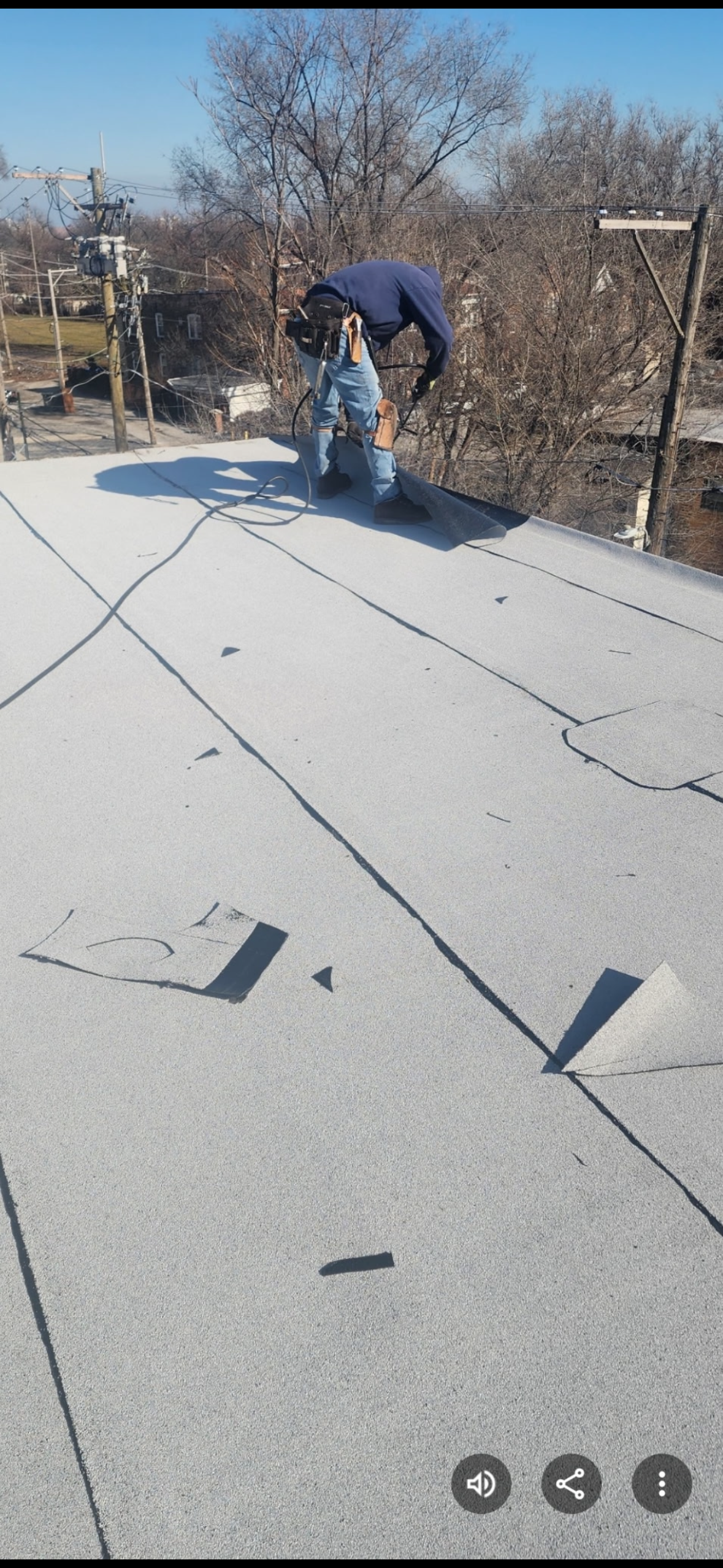 Worker using a blue machine on a flat rooftop under a clear sky