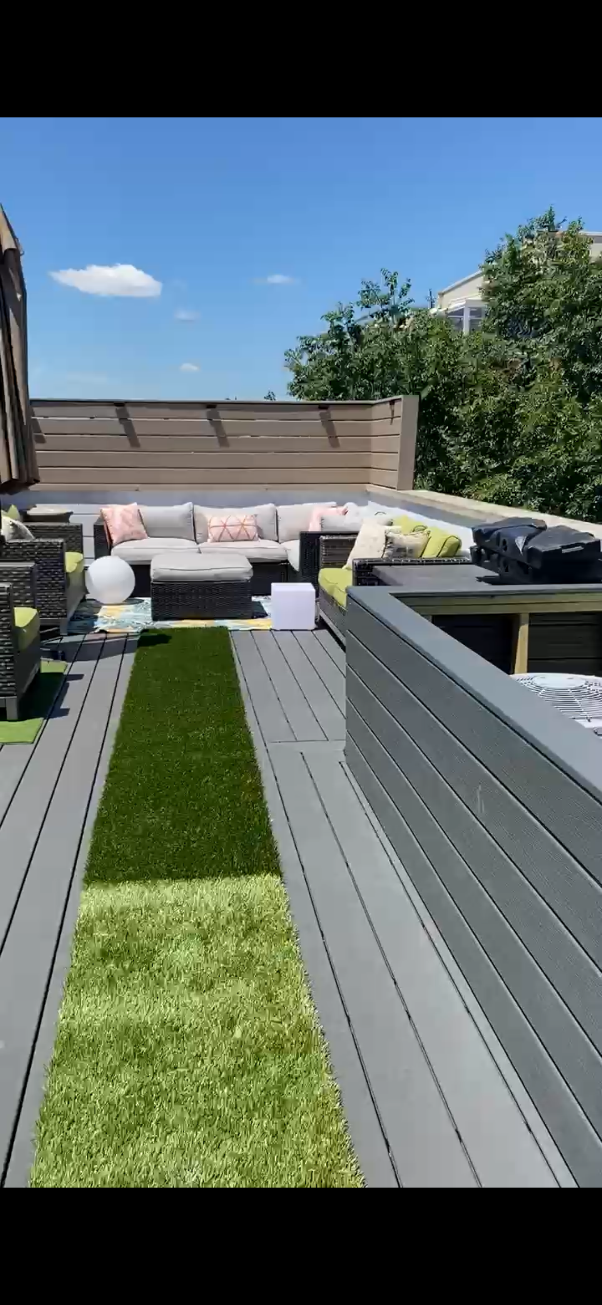 Modern backyard deck with gray flooring, white seating, and green turf under a blue sky