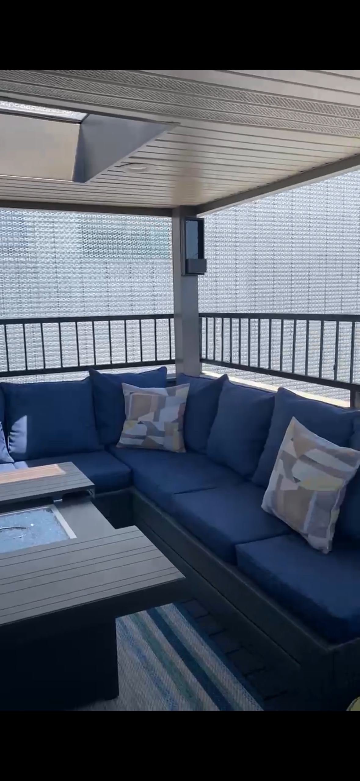 Modern outdoor lounge with dark blue sectional seating, coffee table, and city view behind a railing.