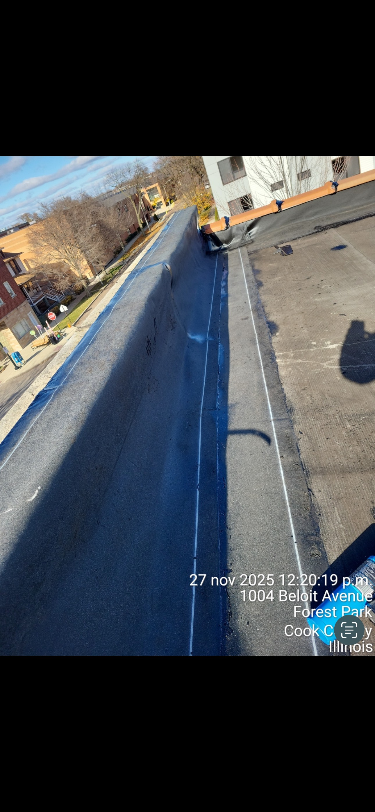 Snow-covered rooftop with blue tarp and long shadow beside a building under a clear sky