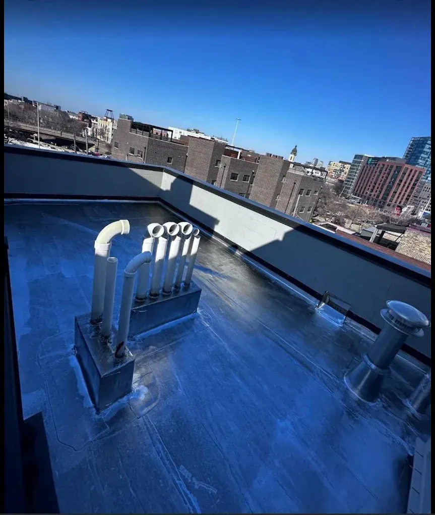 Rooftop with metal vents and blue reflective surface overlooking a city skyline under a clear sky