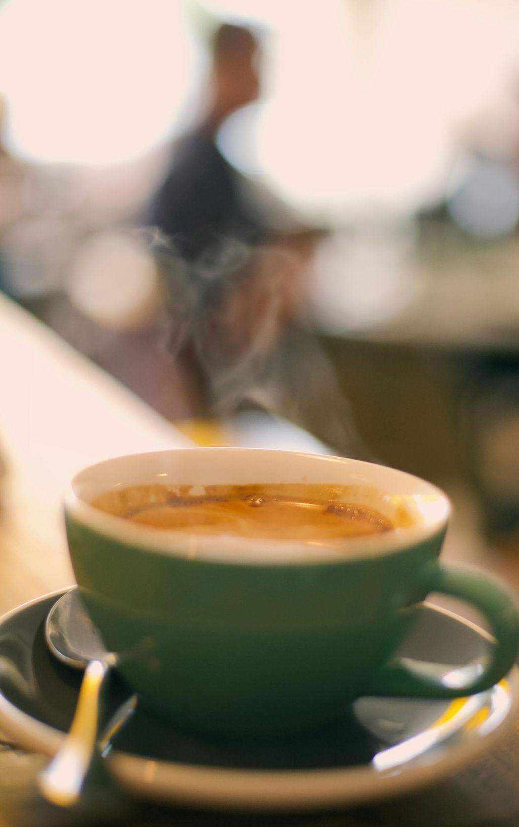 Green coffee cup and saucer on a table with a blurred café background