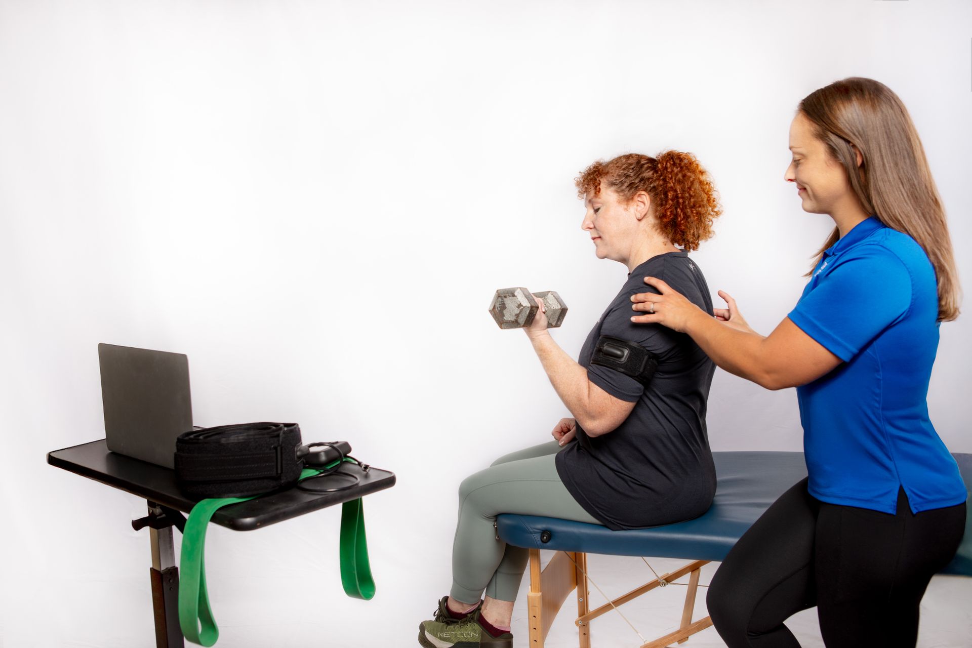 Woman lifting dumbbell with trainer's assistance during a telehealth physical therapy session.