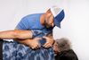 Man adjusting a person's back. The man wears a blue hat and shirt, while the other person is lying down.