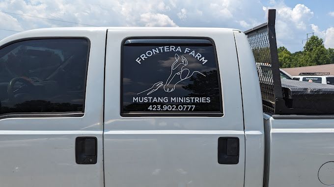 A white truck with a mustang ministries logo on the side of it.