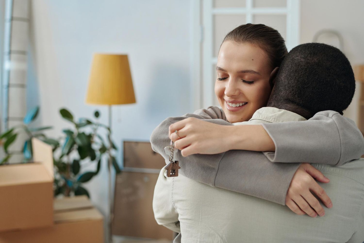 Woman hugging person, holding keys, smiling in a new home with moving boxes.