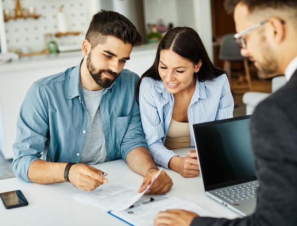 Couple reviewing documents with a financial advisor in a home setting, smiling.
