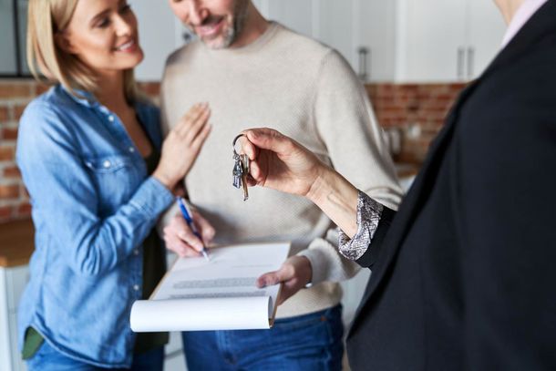 Real estate agent handing keys to a smiling couple after signing a contract.