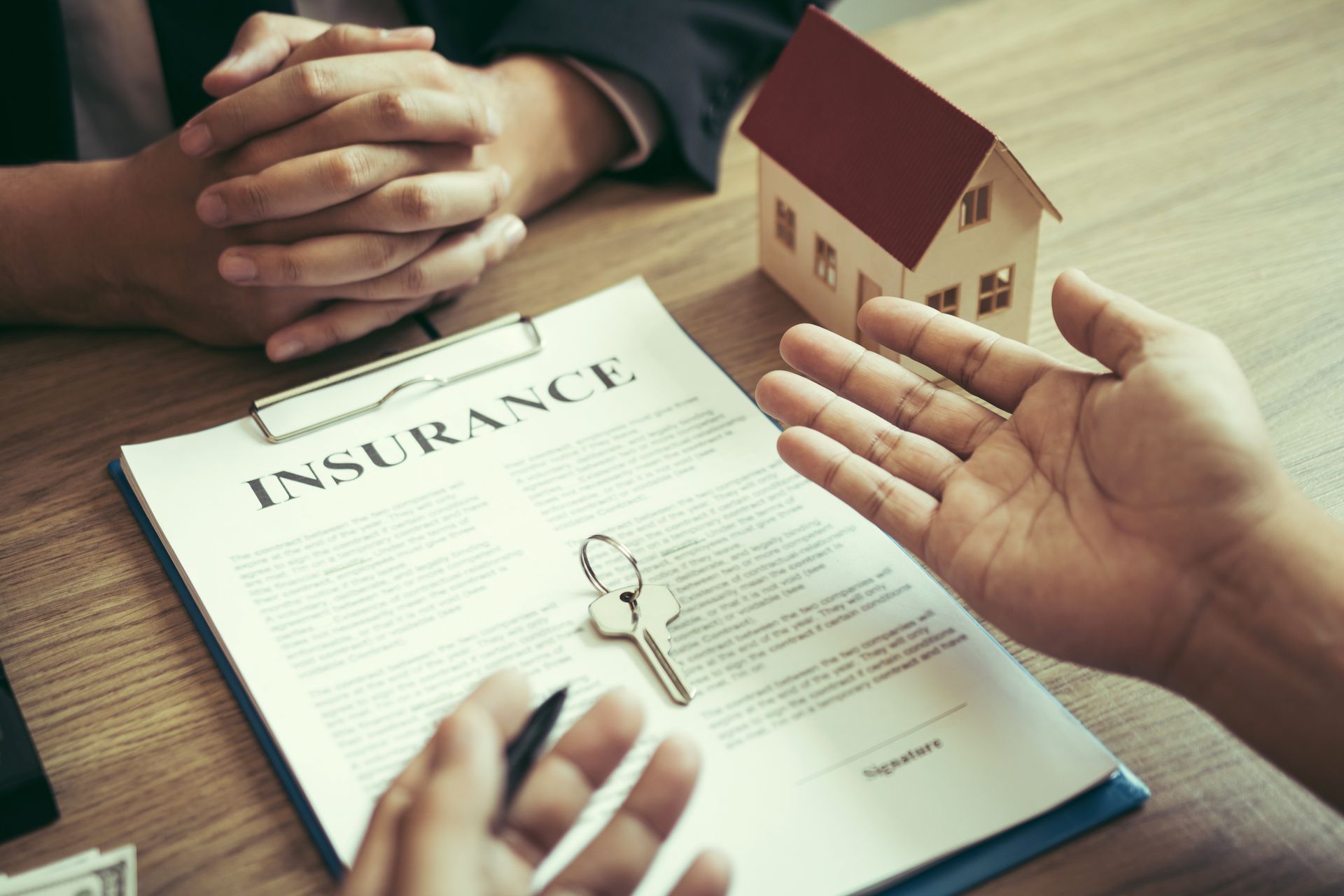 Hands pointing at an insurance document with keys and a house model.
