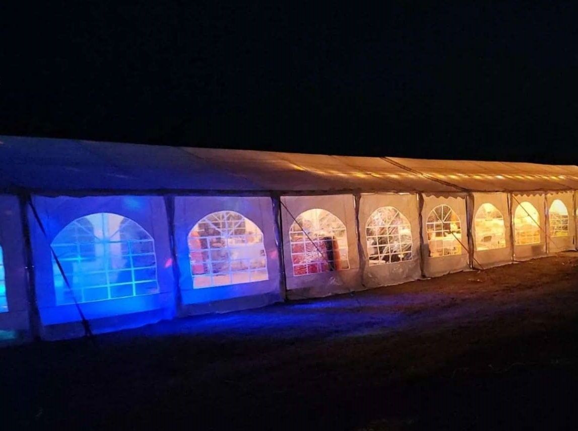 A row of tents are lit up at night with blue lights.