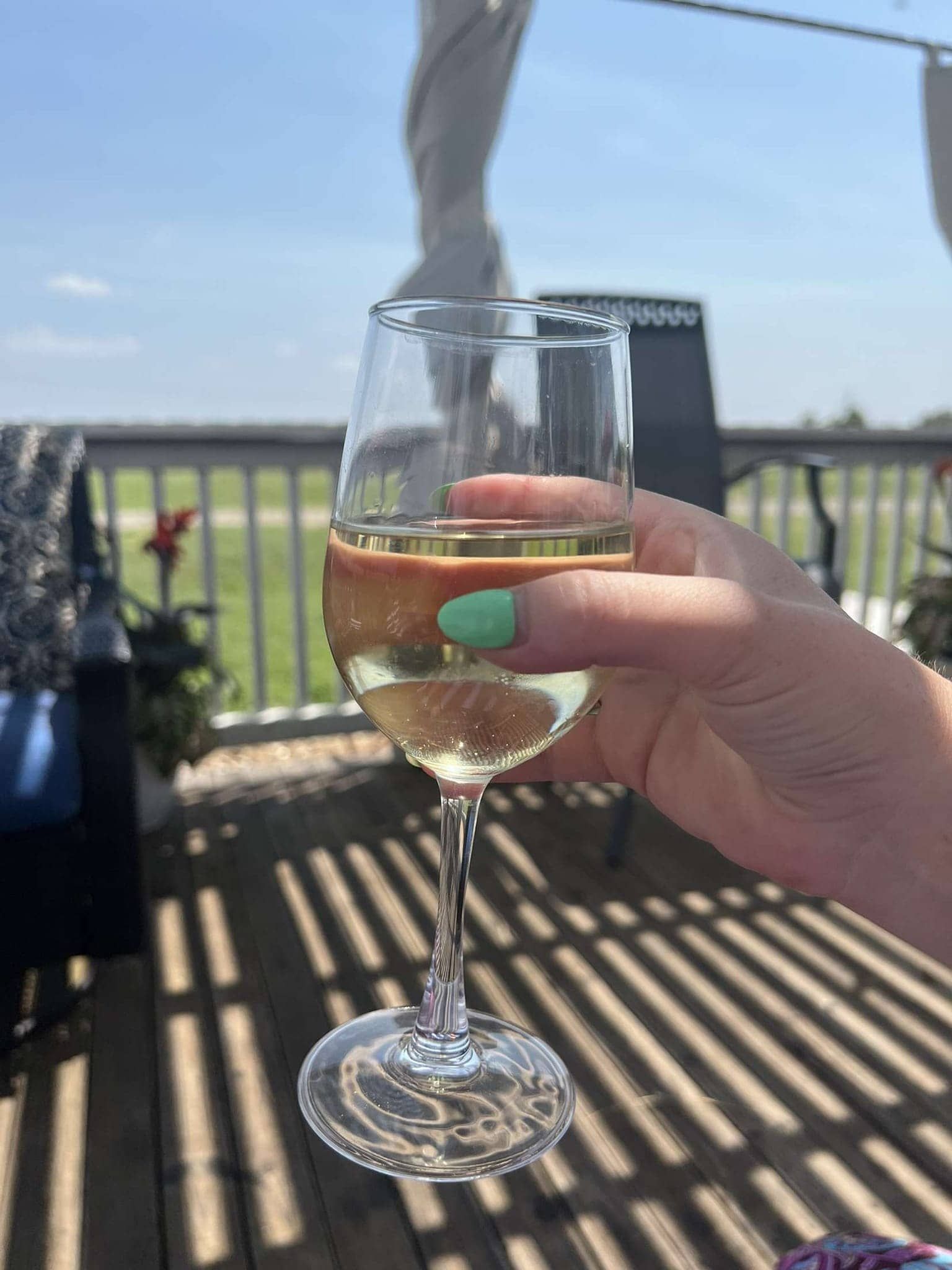 A woman is holding a glass of wine on a winery deck overlooking a vineyard.
