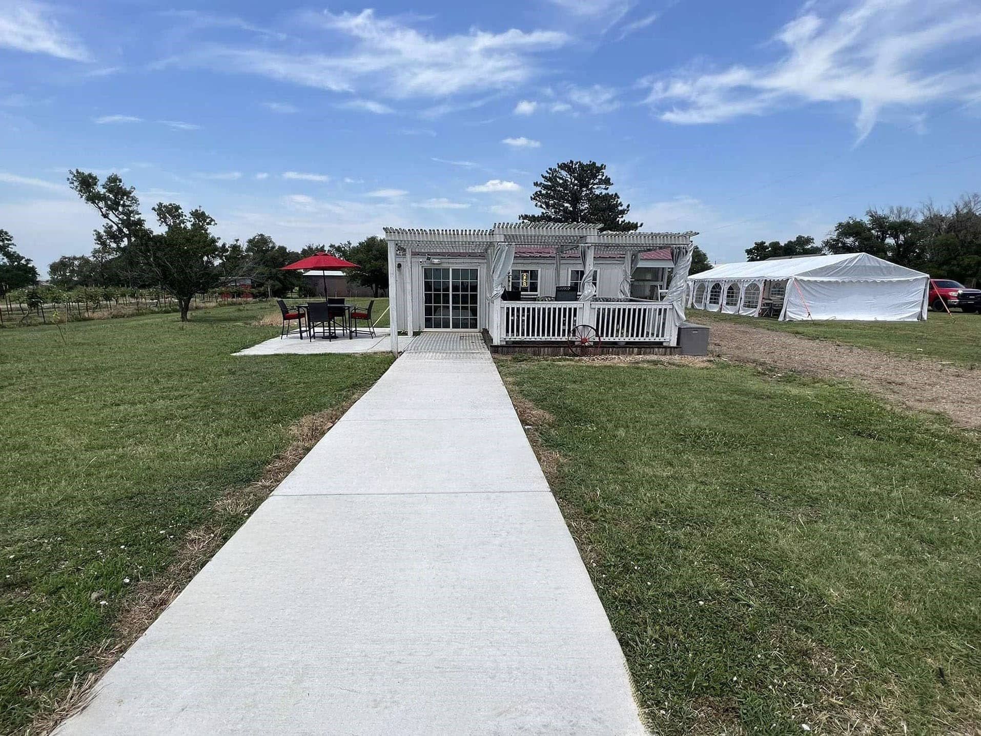 A white house winery with a patio and concrete walkway leading to it.