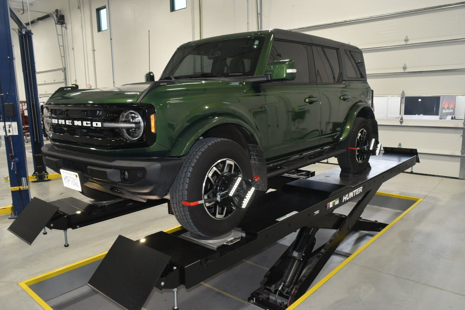 Dark green Ford Bronco on a vehicle lift in an auto shop indoors.