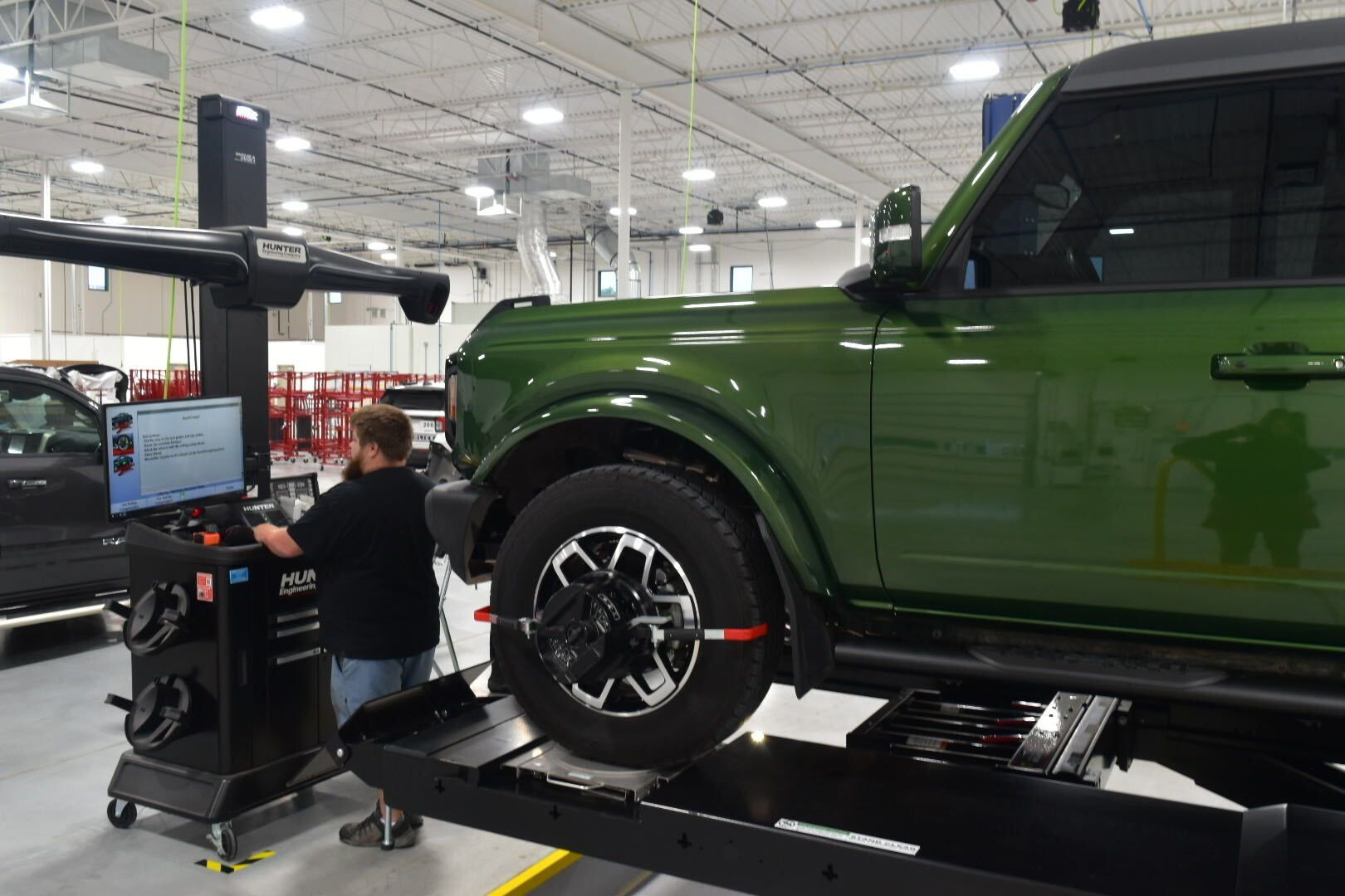 Green SUV on a lift in an auto shop while a mechanic works on a wheel alignment machine