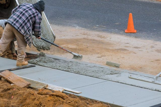 A man is pouring concrete on a sidewalk with a shovel.