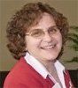 A woman wearing glasses and a red sweater is smiling for the camera.