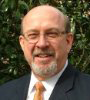 A bald man with a beard and glasses is wearing a suit and tie.