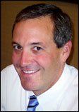 A man in a white shirt and blue tie is smiling for the camera.