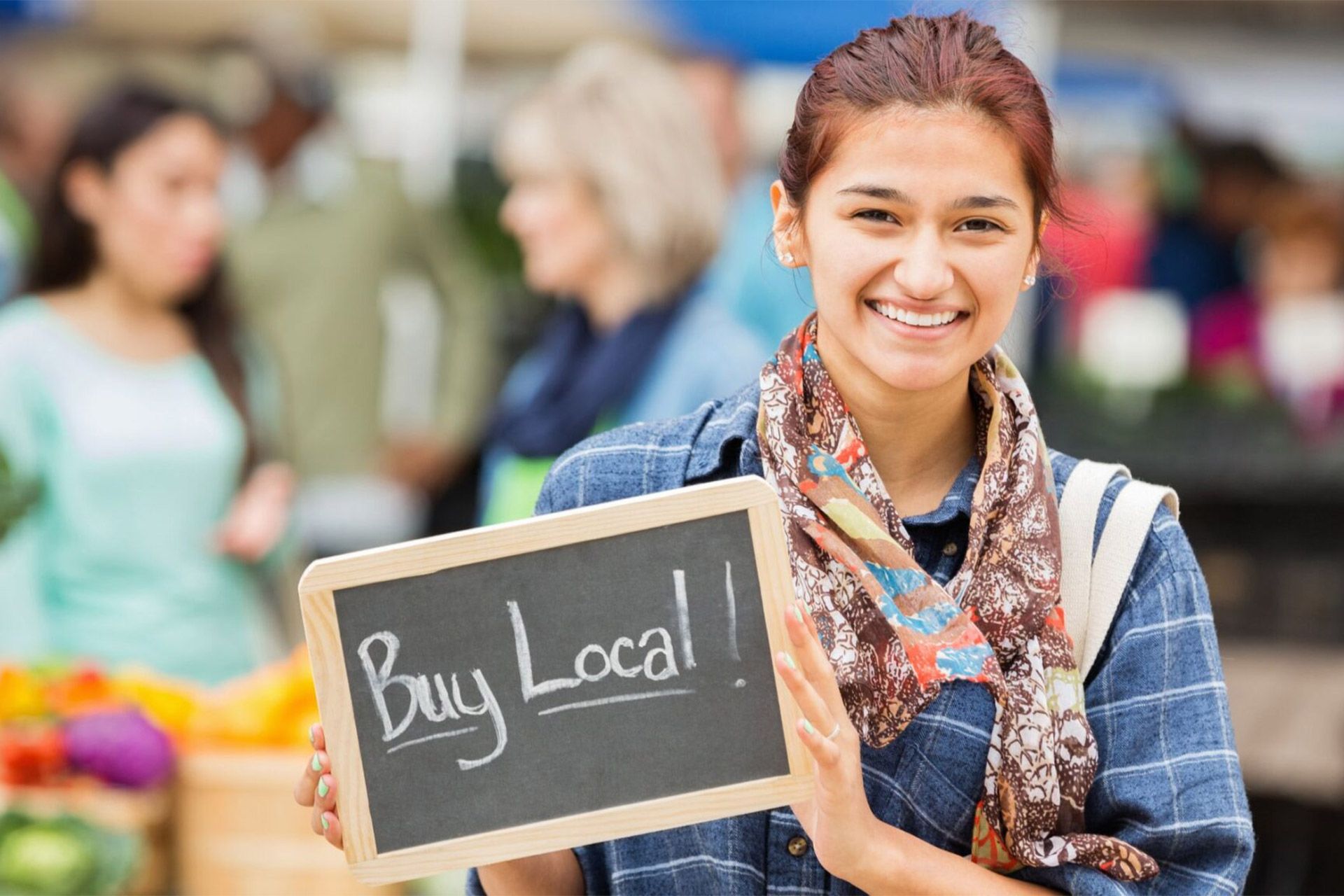 Woman at a farmers market holds a sign that says
