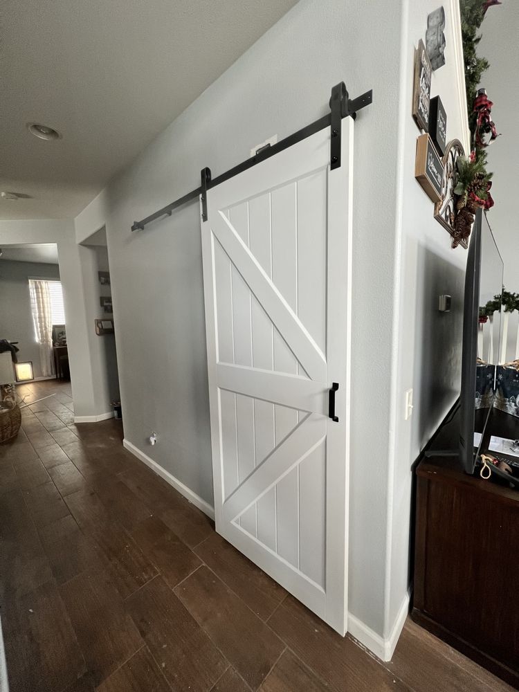 White barn door on a gray wall with black hardware, in a hallway with wooden floors.
