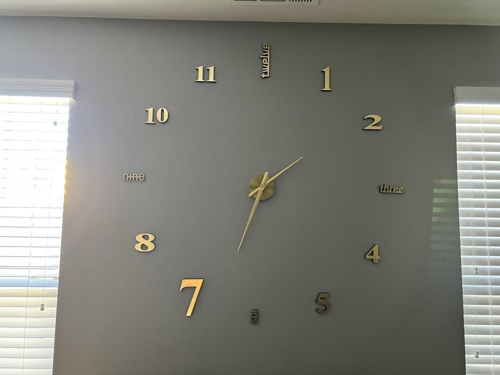 A large, gold-colored wall clock with numerals on a gray wall.