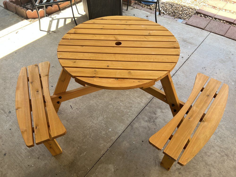 Wooden round picnic table with two attached benches, outdoors.