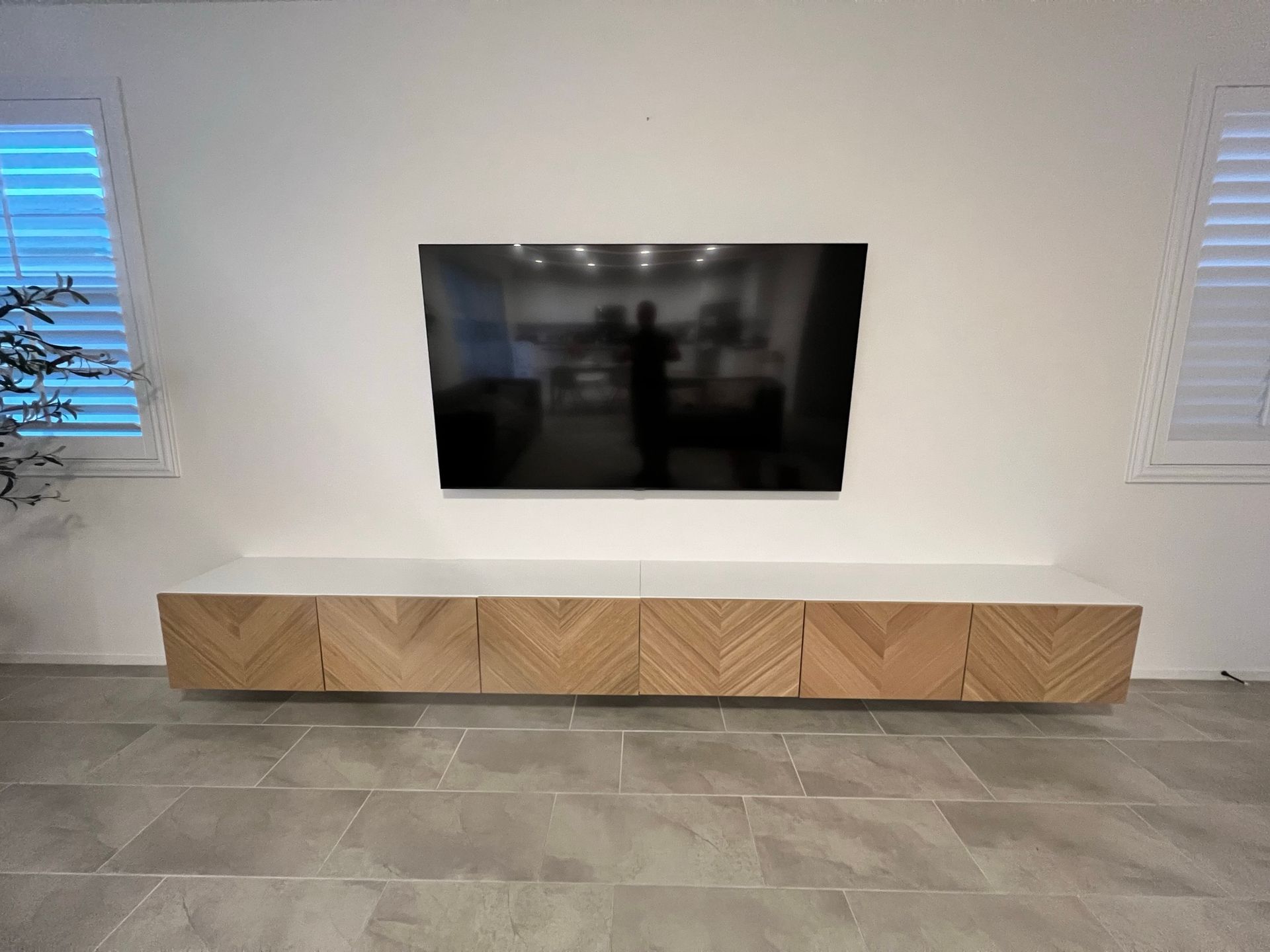 Floating TV and cabinet on a white wall, with a herringbone pattern on the cabinet doors and gray tiled floor.