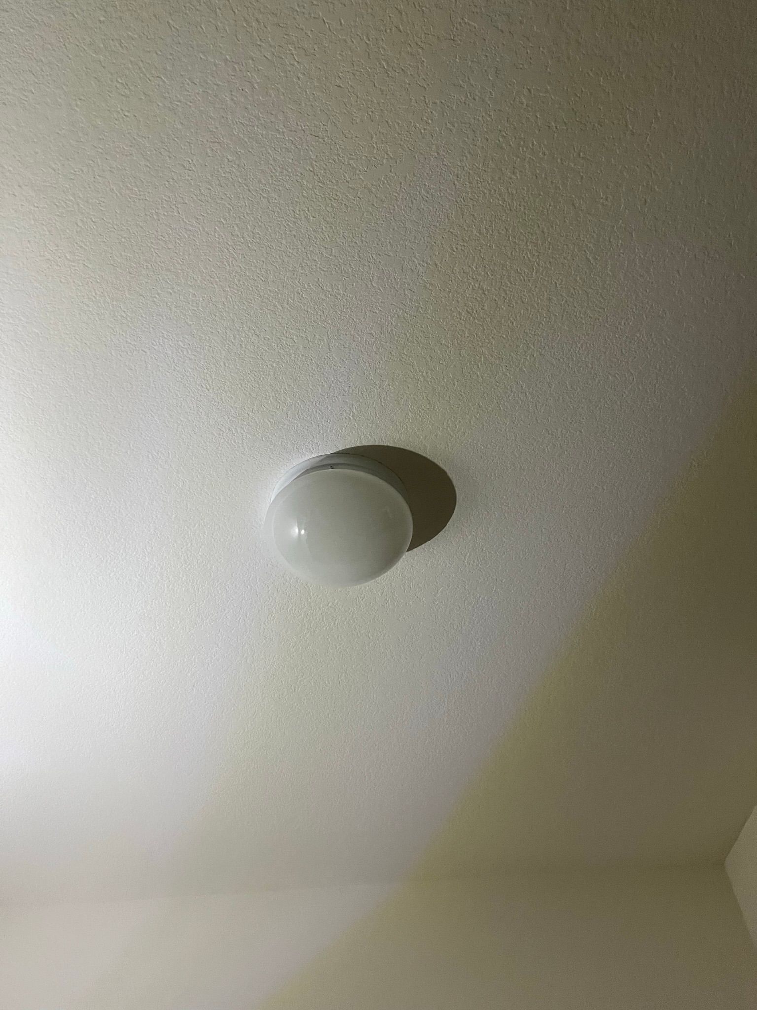Ceiling with a round, white light fixture casting a shadow.